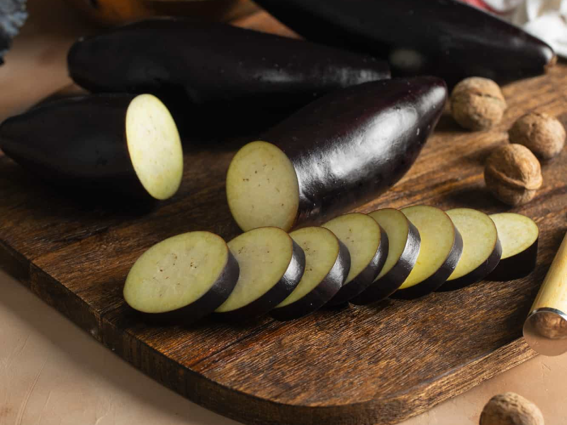 Circle-shaped cut eggplant on a wooden cutting board, showing preparation for serving eggplant to dogs.